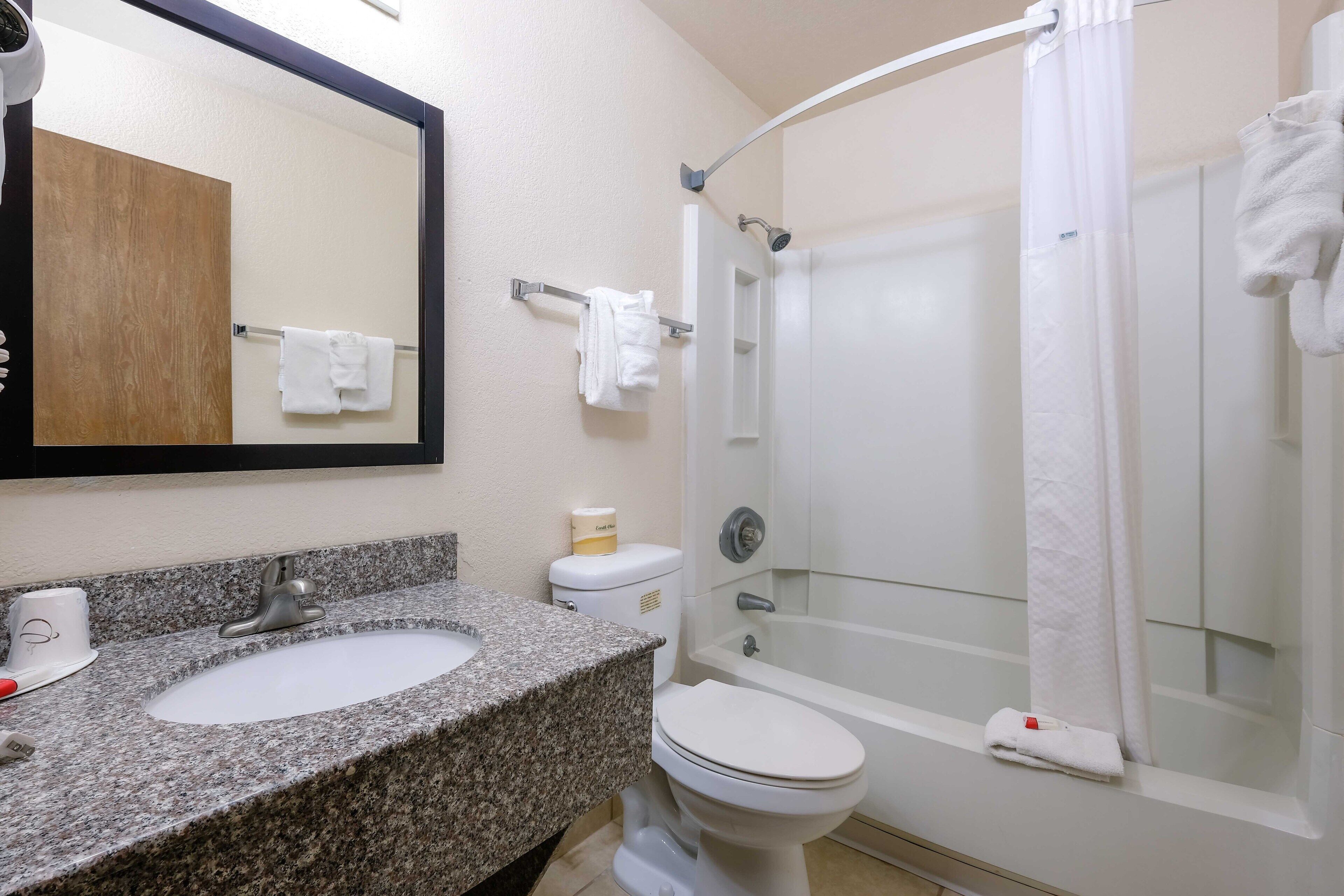 A bathroom with a granite sink, white toilet, and a glass-enclosed shower.