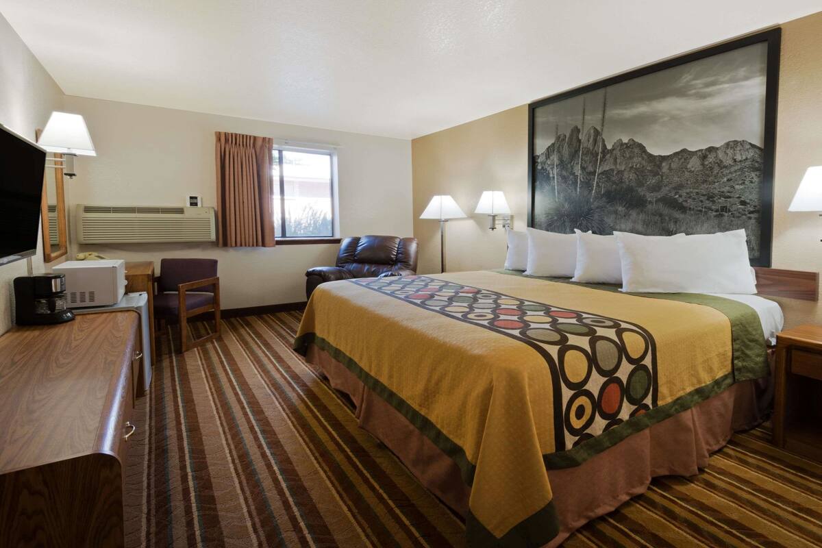Habitación de hotel con una cama grande, un escritorio con lámpara, una silla, un televisor y un cuadro en la pared.