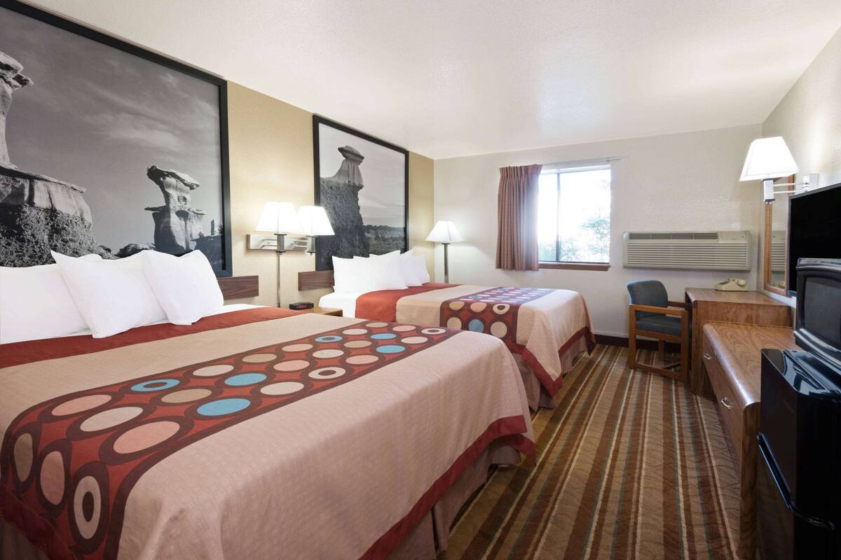 Habitación de hotel con dos camas, televisión, escritorio y ventana con cortinas.