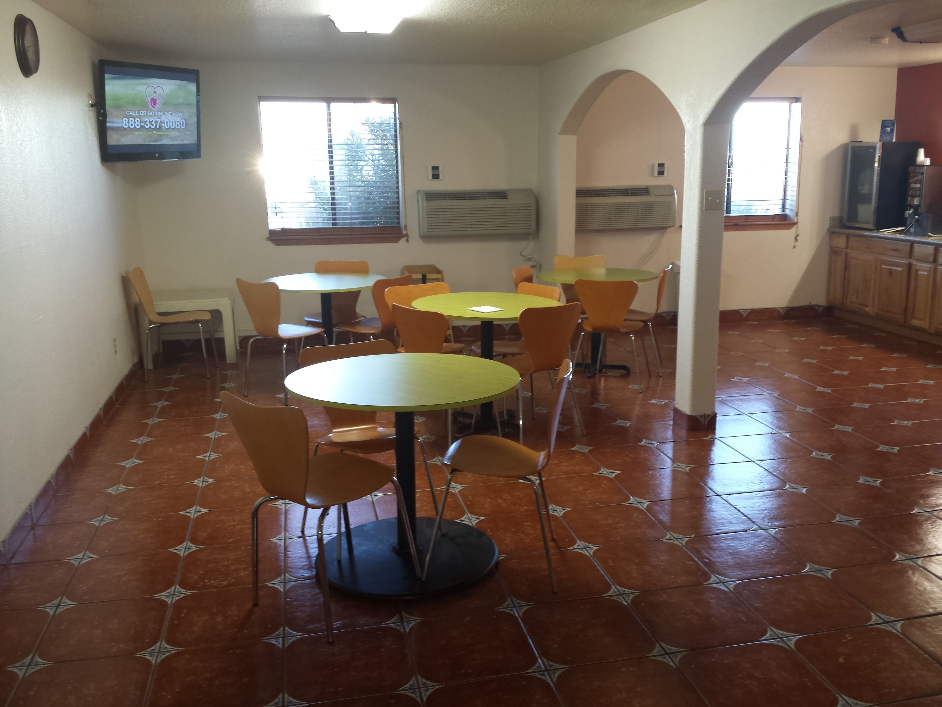 Un espace repas comprenant plusieurs tables rondes et des chaises, des unités de climatisation et un téléviseur fixé au mur.