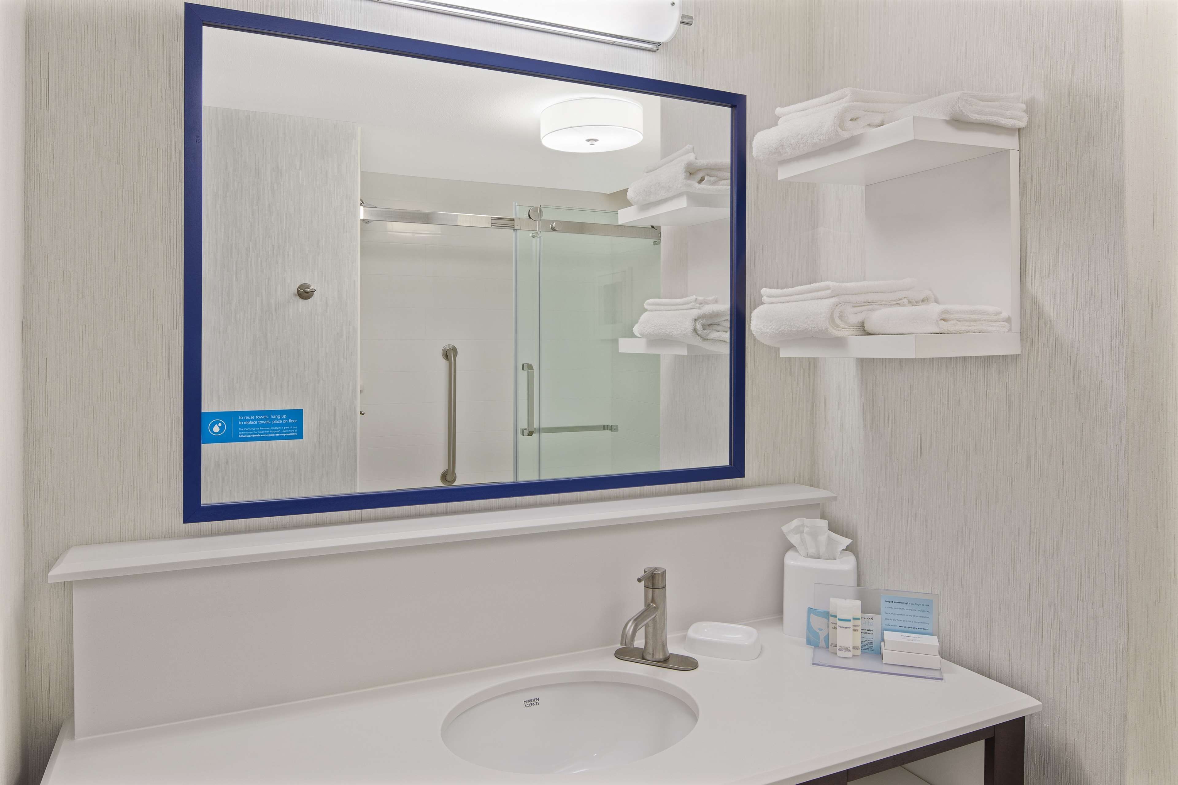 A bathroom with a large mirror, a sink, and a towel rack.