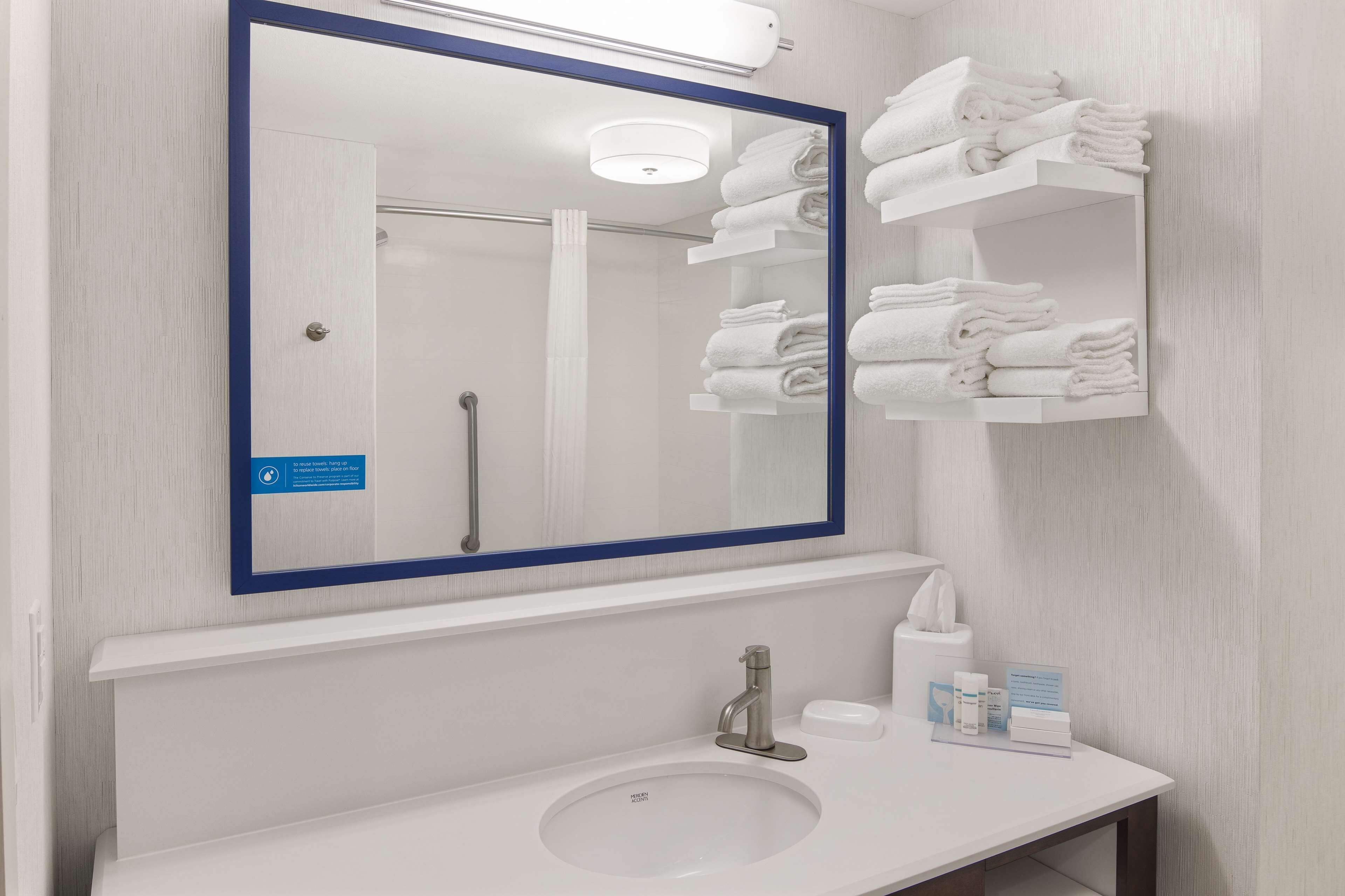 Un baño con un espejo grande, un lavabo y un perchero con toallas dobladas.