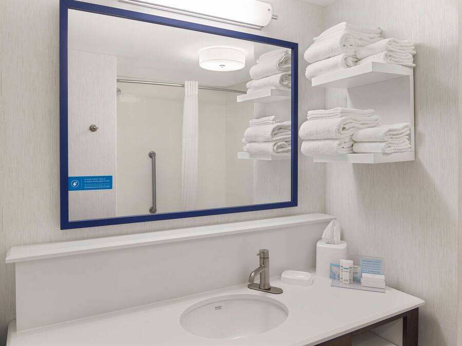 A bathroom with a large mirror, a sink, and a towel rack with folded towels.