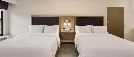 A hotel room with two beds, a bedside table with a lamp, a wooden headboard, and a door.