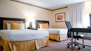 A hotel room with two beds, a desk, a chair, a lamp, and a painting on the wall.