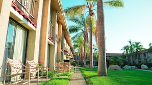 A hotel corridor with a pathway, palm trees, and outdoor seating.