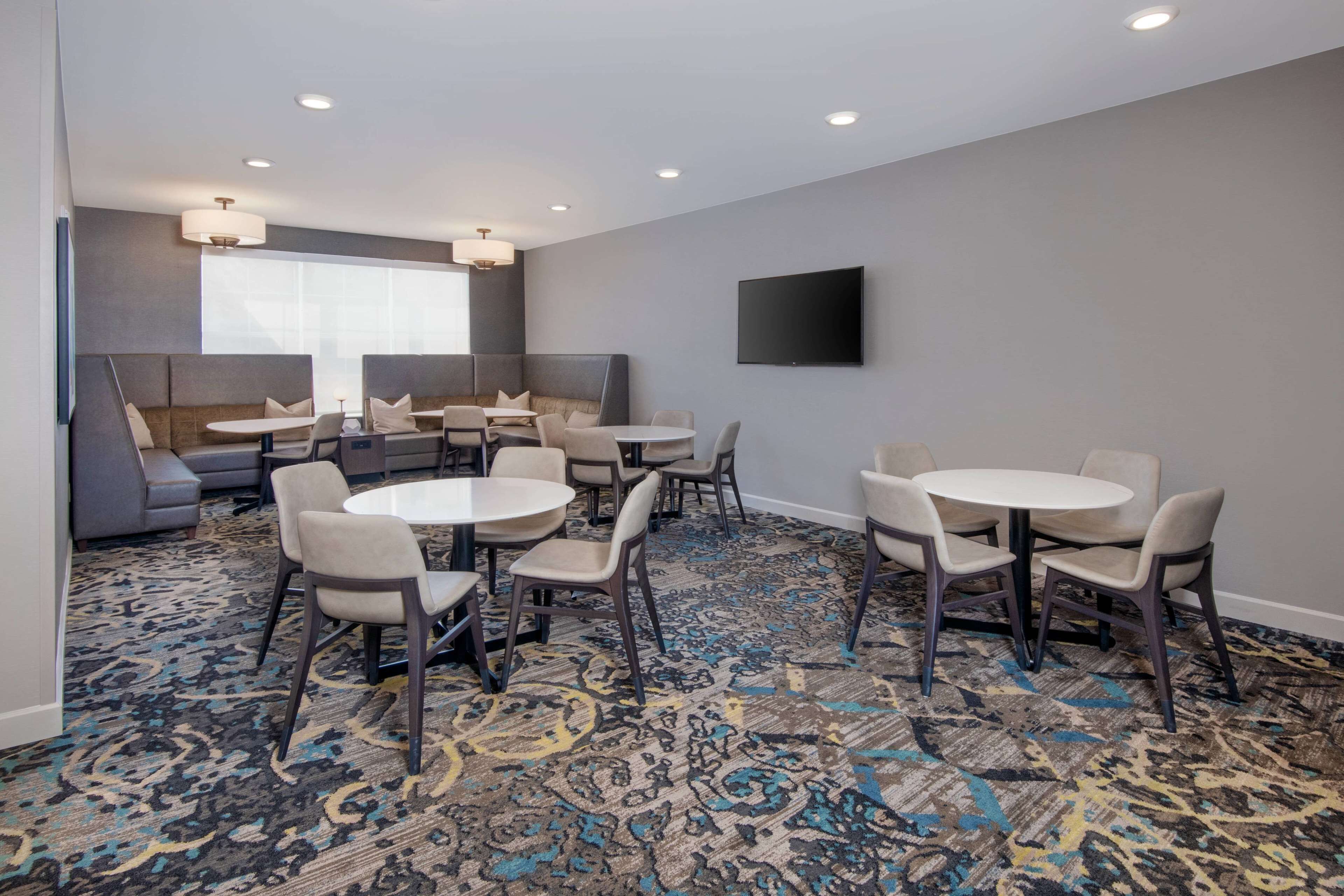 A hotel room with a large window, a flat-screen TV mounted on the wall, and a carpeted floor.