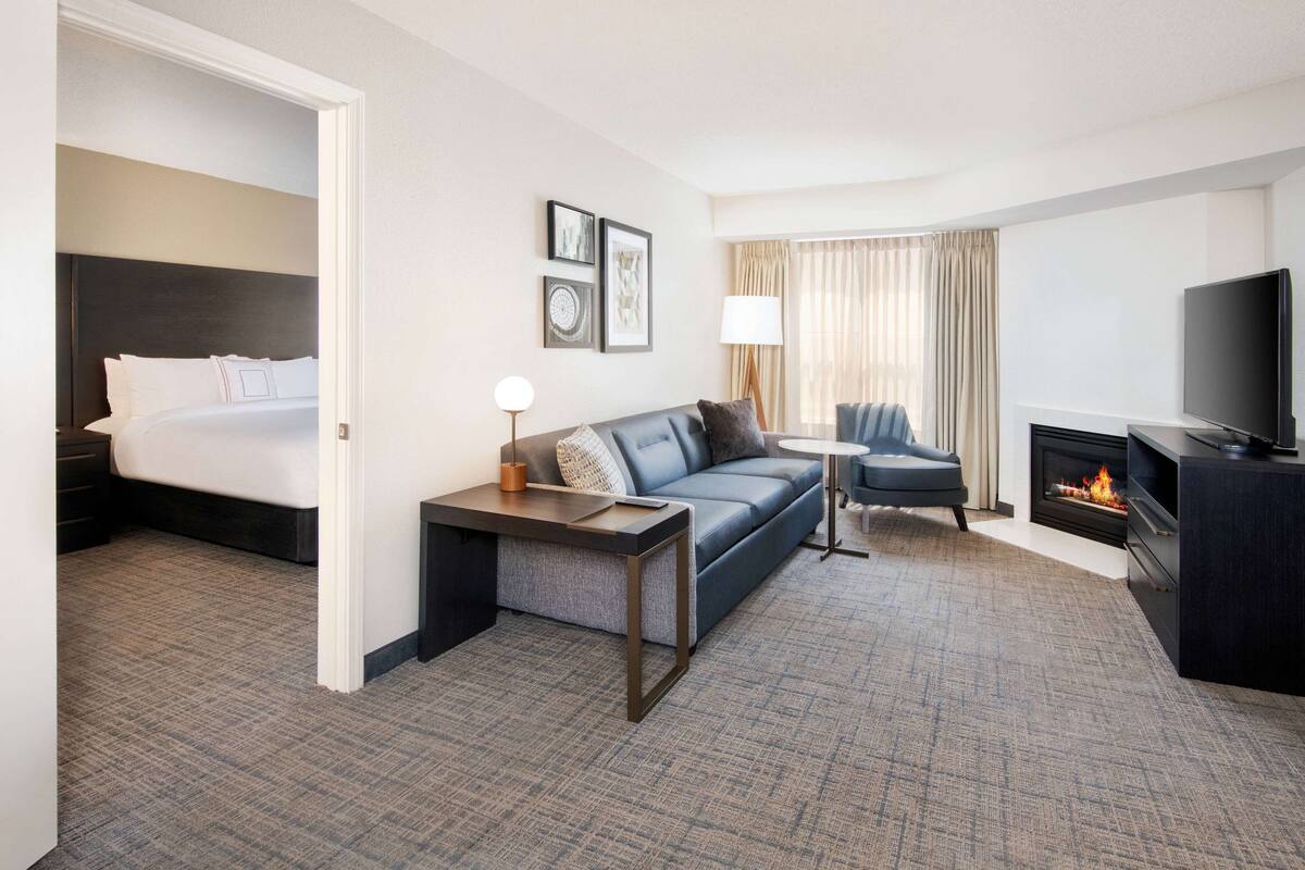 Una habitación de hotel con cama, sofá, televisión, chimenea y una mesita con lámpara.