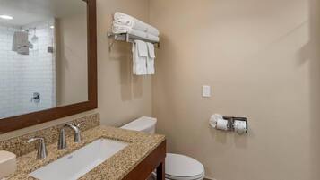A bathroom with a granite countertop, two sinks, a toilet, a towel rack, and a mirror.