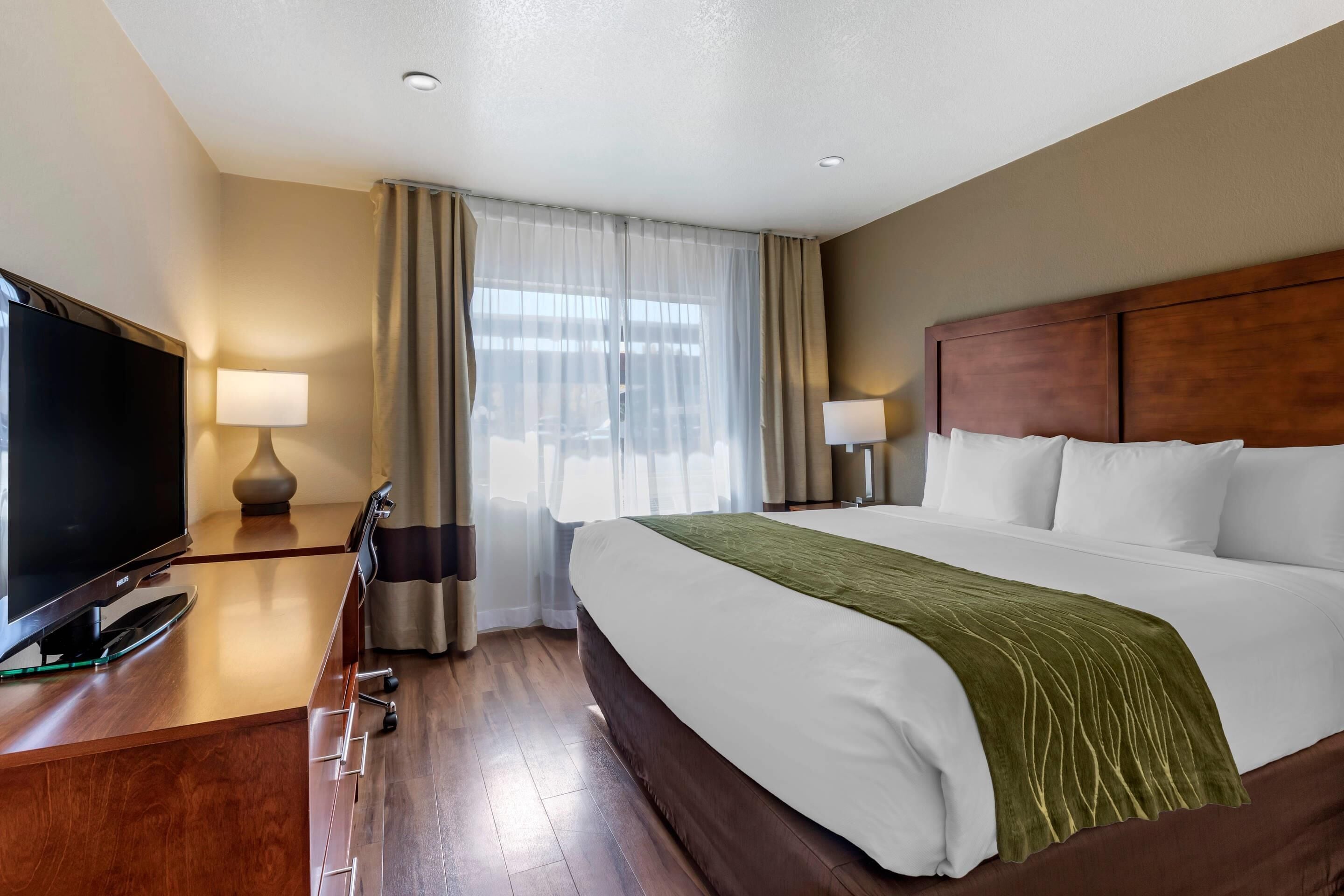 Una habitación de hotel con cama, televisión sobre un escritorio y ventana con cortinas.