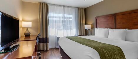 Una habitación de hotel con cama, televisión sobre un escritorio y ventana con cortinas.