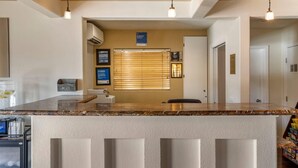 A kitchen with a marble countertop, a refrigerator, a mail slot, and a window with blinds.