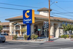 A Comfort Inn hotel with a prominent blue and yellow sign, a two-story building with a brown roof, and a street view with traffic lights and a parked car.