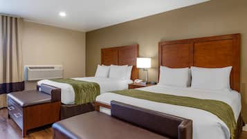 A hotel room with two beds, a desk, a chair, a lamp, and an air conditioning unit.