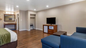 A hotel room with a bed, a TV, a sofa, a small cabinet, and a mirror.