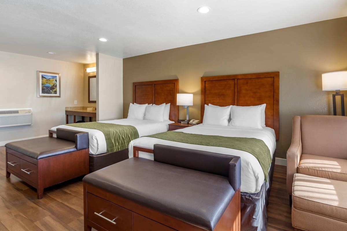 A hotel room with two beds, a desk, a chair, and a small table.