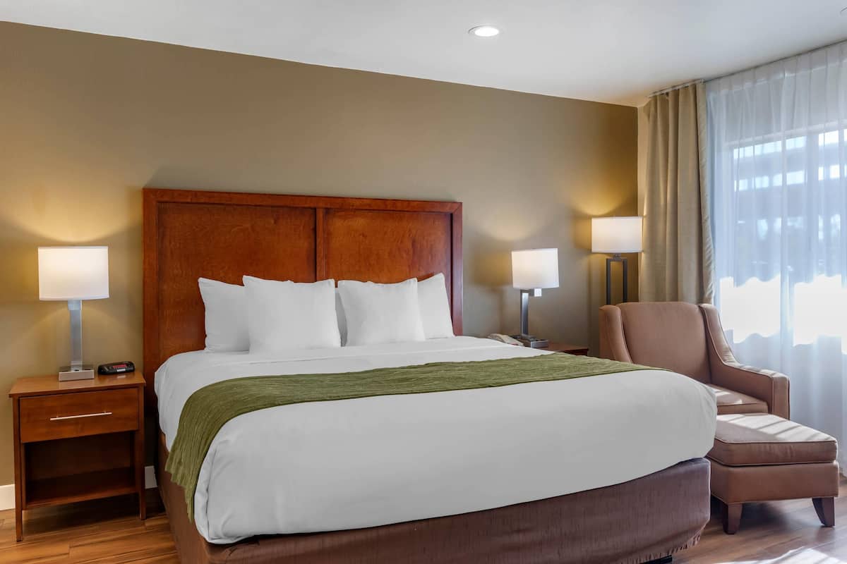 A hotel room with a large bed, two bedside tables with lamps, a chair, and a window with curtains.