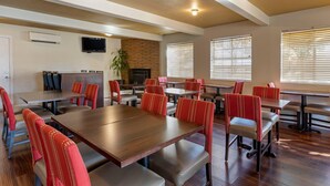 A dining area with multiple tables and chairs, a television mounted on the wall, and a brick fireplace.