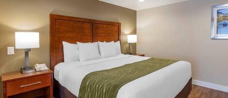 Habitación de hotel con una cama grande, cabecera de madera, lámparas de noche, mesita de noche con teléfono y un cuadro en la pared.