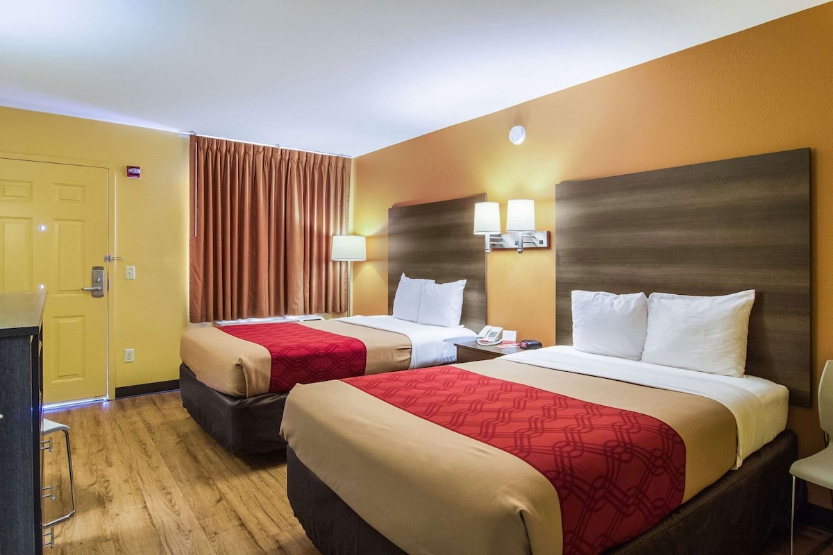 A hotel room with two beds, a desk, a chair, a telephone, and a wall-mounted lamp.