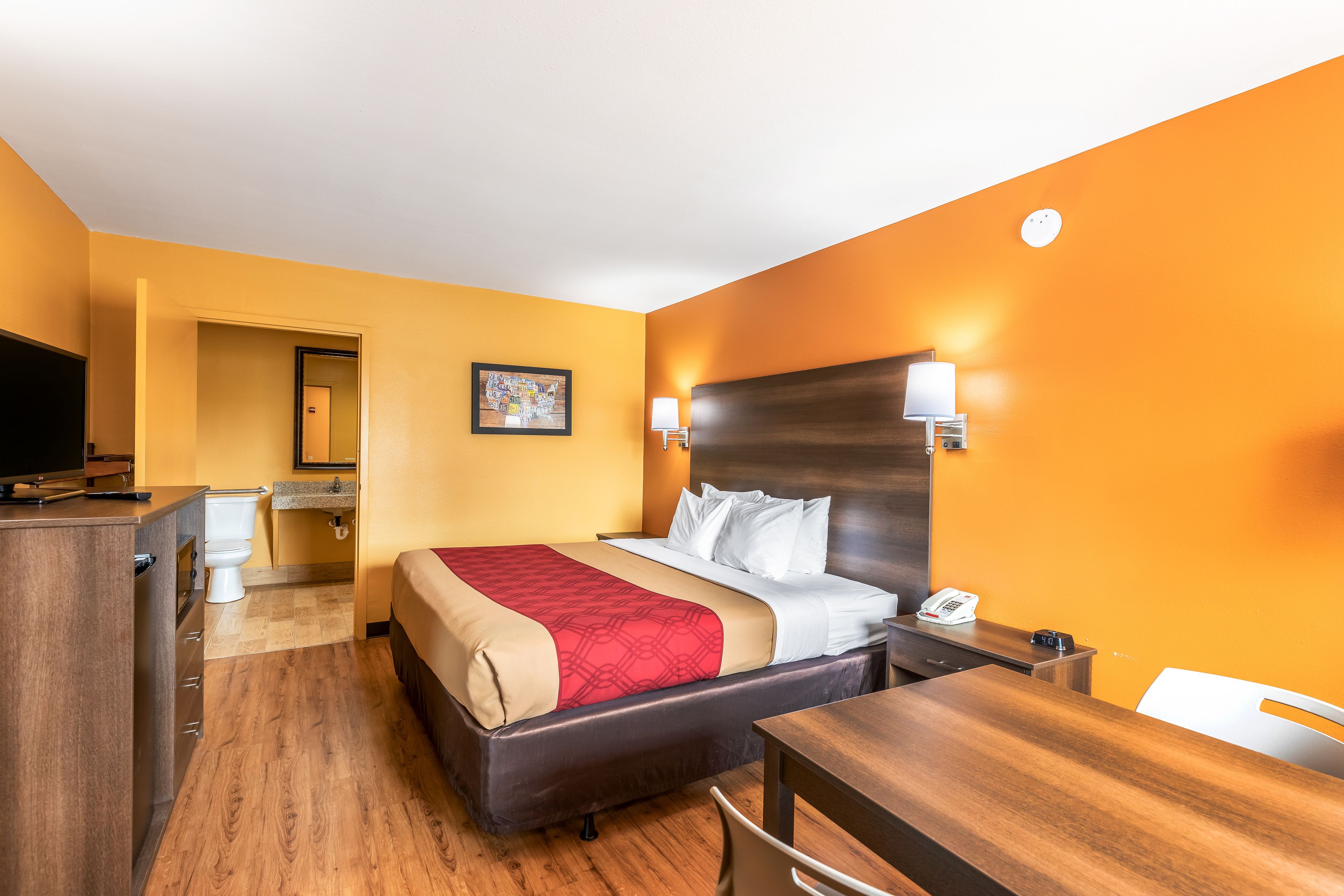 A hotel room with a bed, desk, chair, and a bathroom visible through an open door.