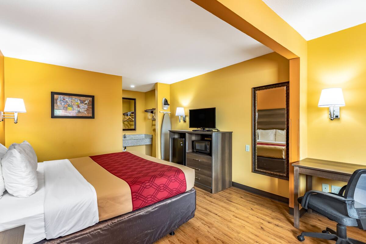 A hotel room with a bed, desk, TV, and a mirror.
