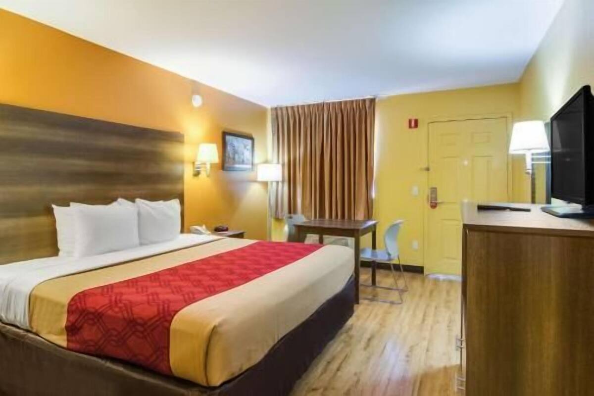 A hotel room with a bed, a desk, a chair, a television, and a door.