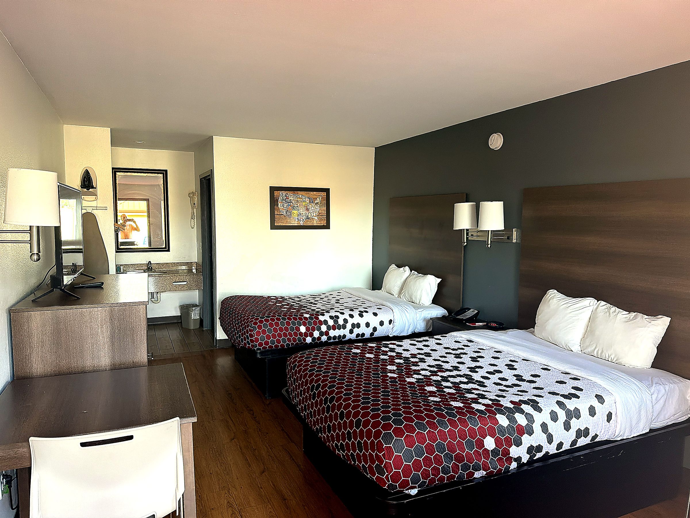 Een hotelkamer met twee bedden, een bureau, een stoel, een badkamer en een wandlamp.