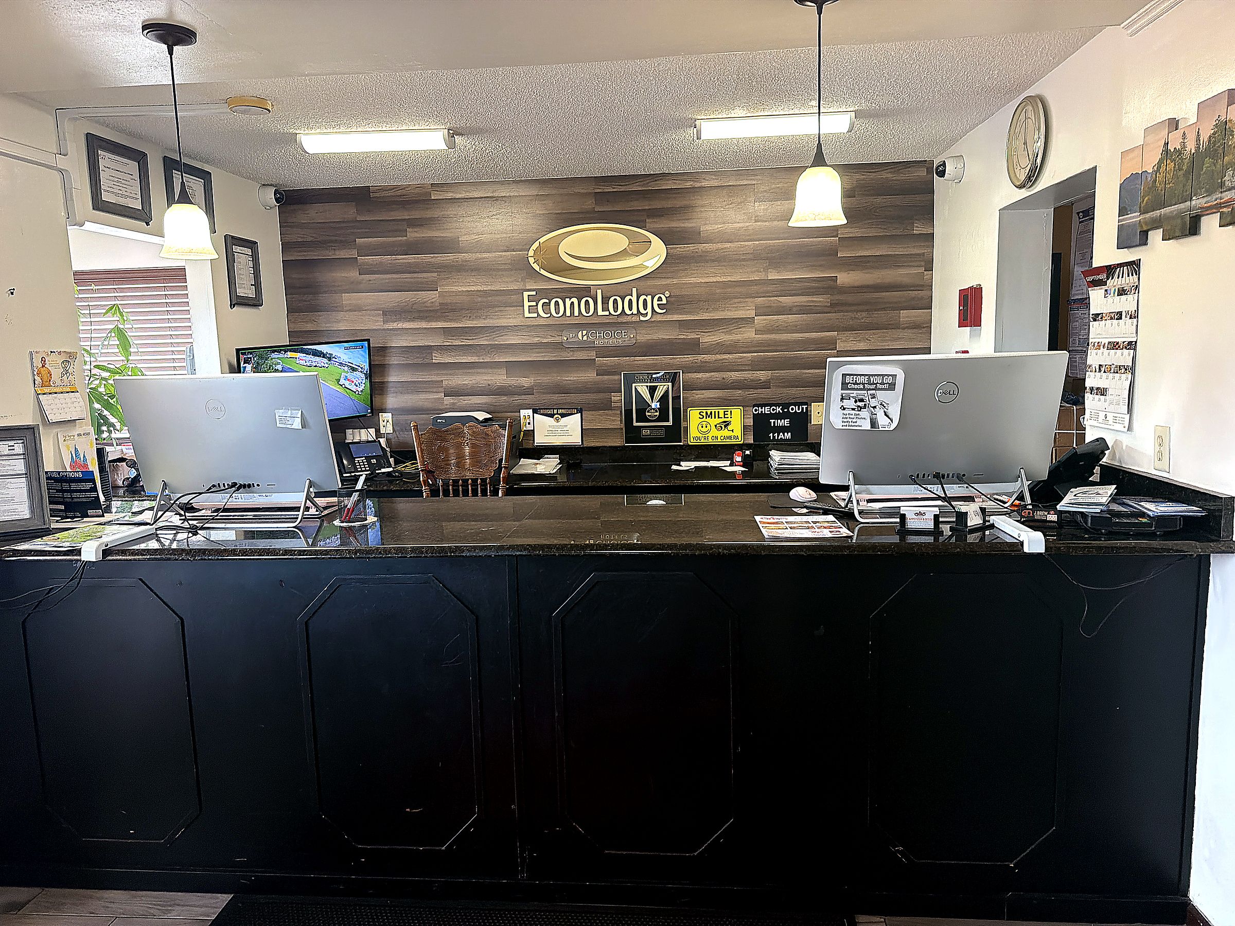 A reception desk at Ecolodge with a wooden backdrop, two computer monitors, a clock, and framed pictures on the wall.