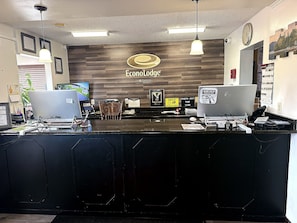 A reception desk at Ecolodge with a wooden backdrop, two computer monitors, a clock, and framed pictures on the wall. - Econo Lodge Kingsland (Kingsland)