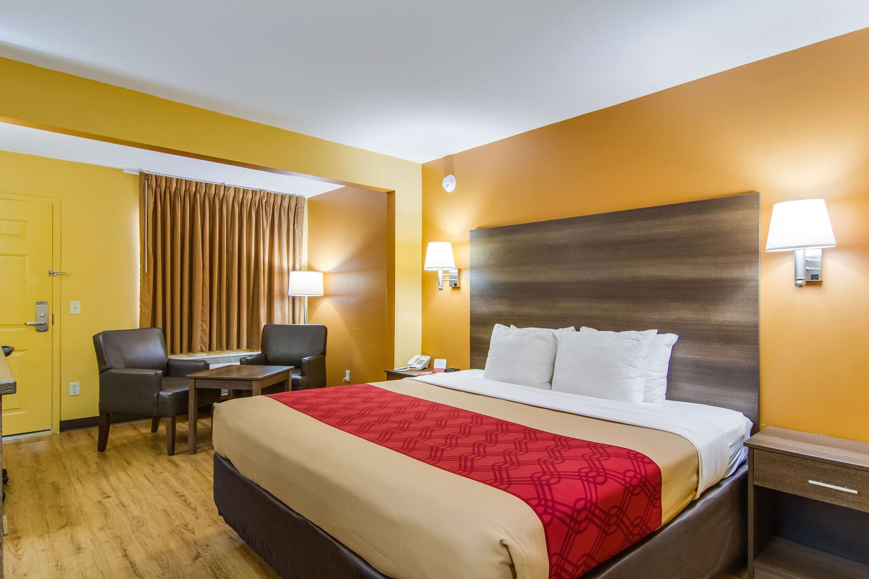 A hotel room with a bed, a desk, a chair, a nightstand, and a lamp.