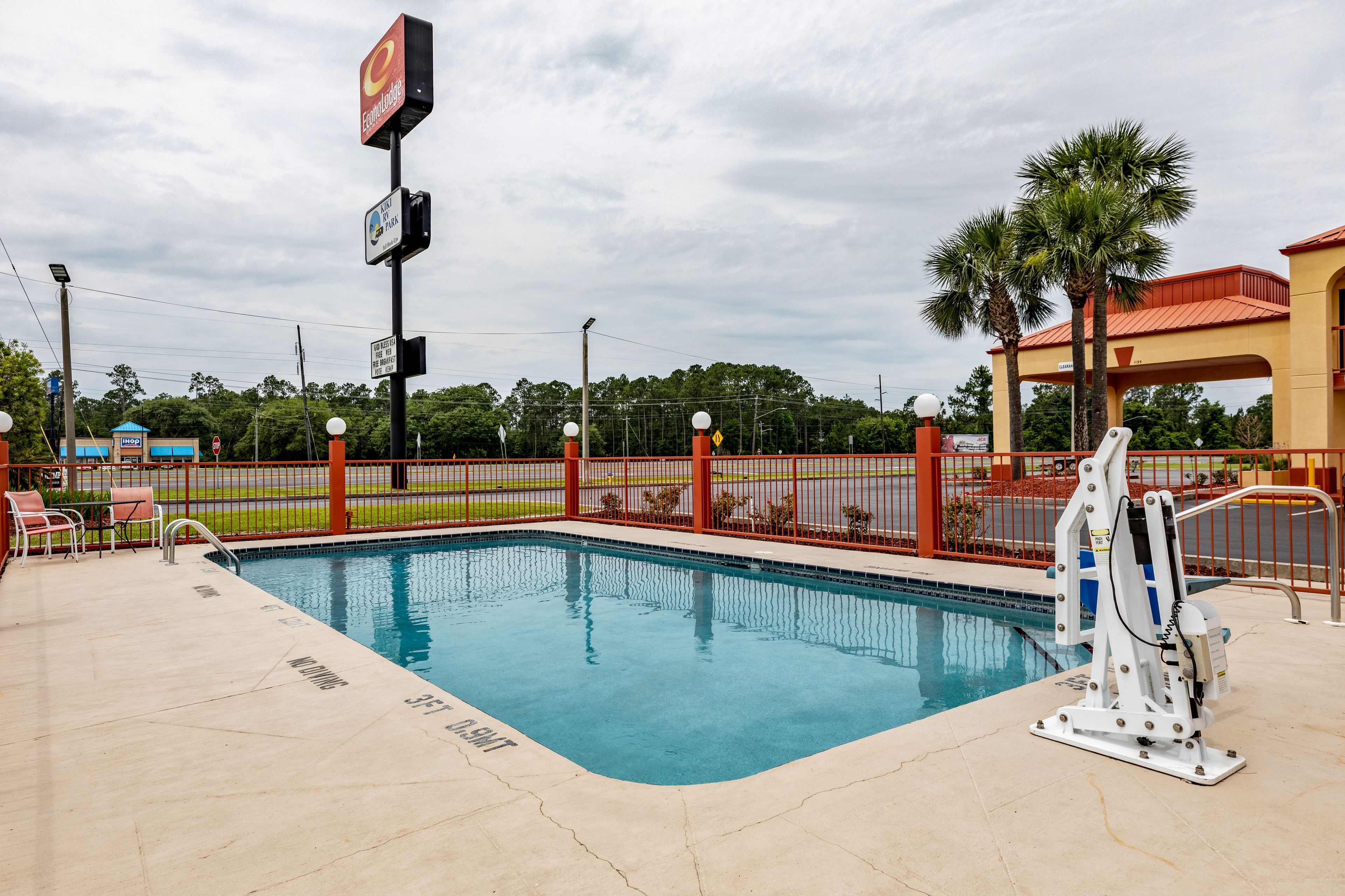 A swimming pool with a lifeguard stand, a fenced area, and a building with a red roof in the background.