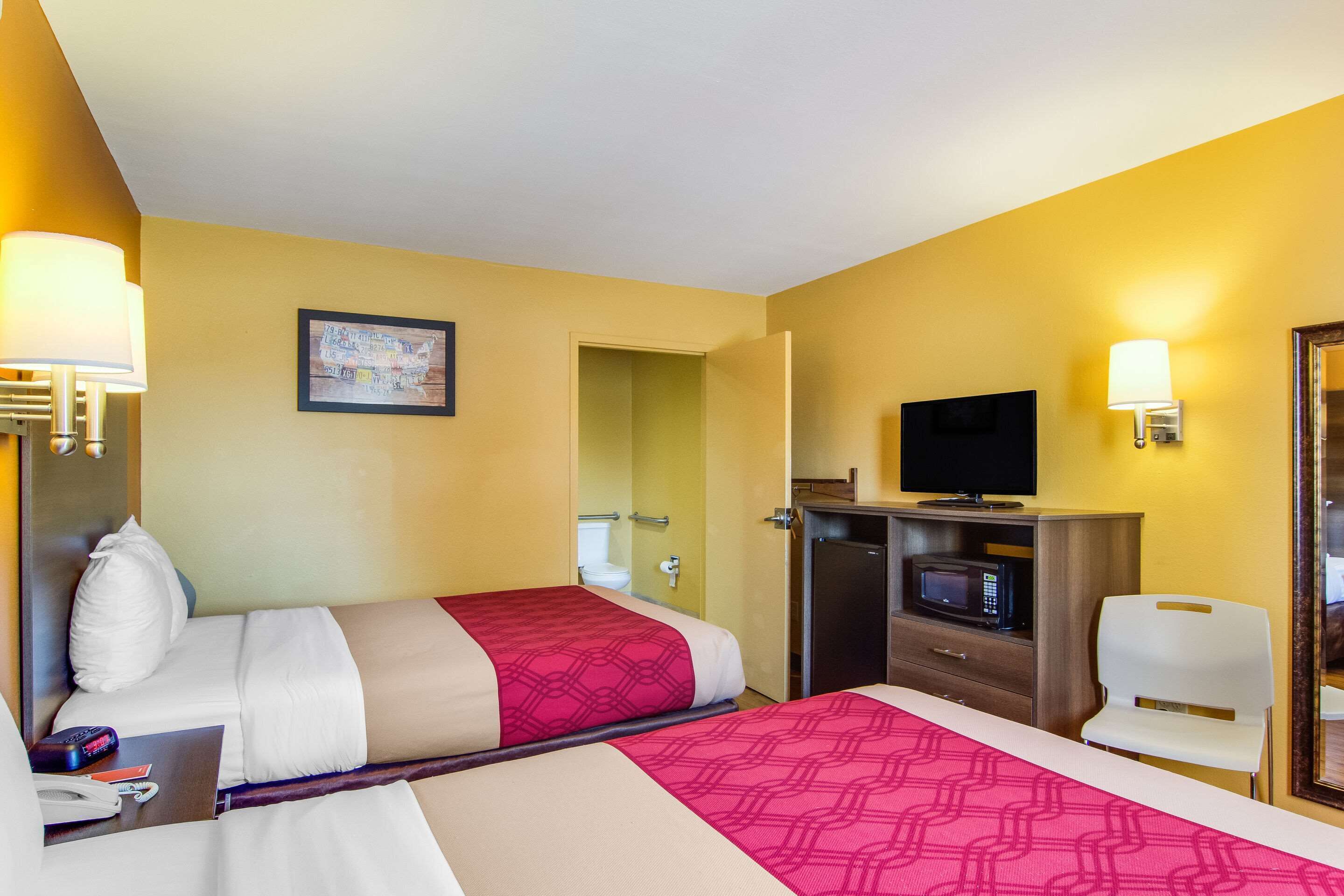 A hotel room with two beds, a desk with a telephone and remote controls, a microwave, a television, and a chair.
