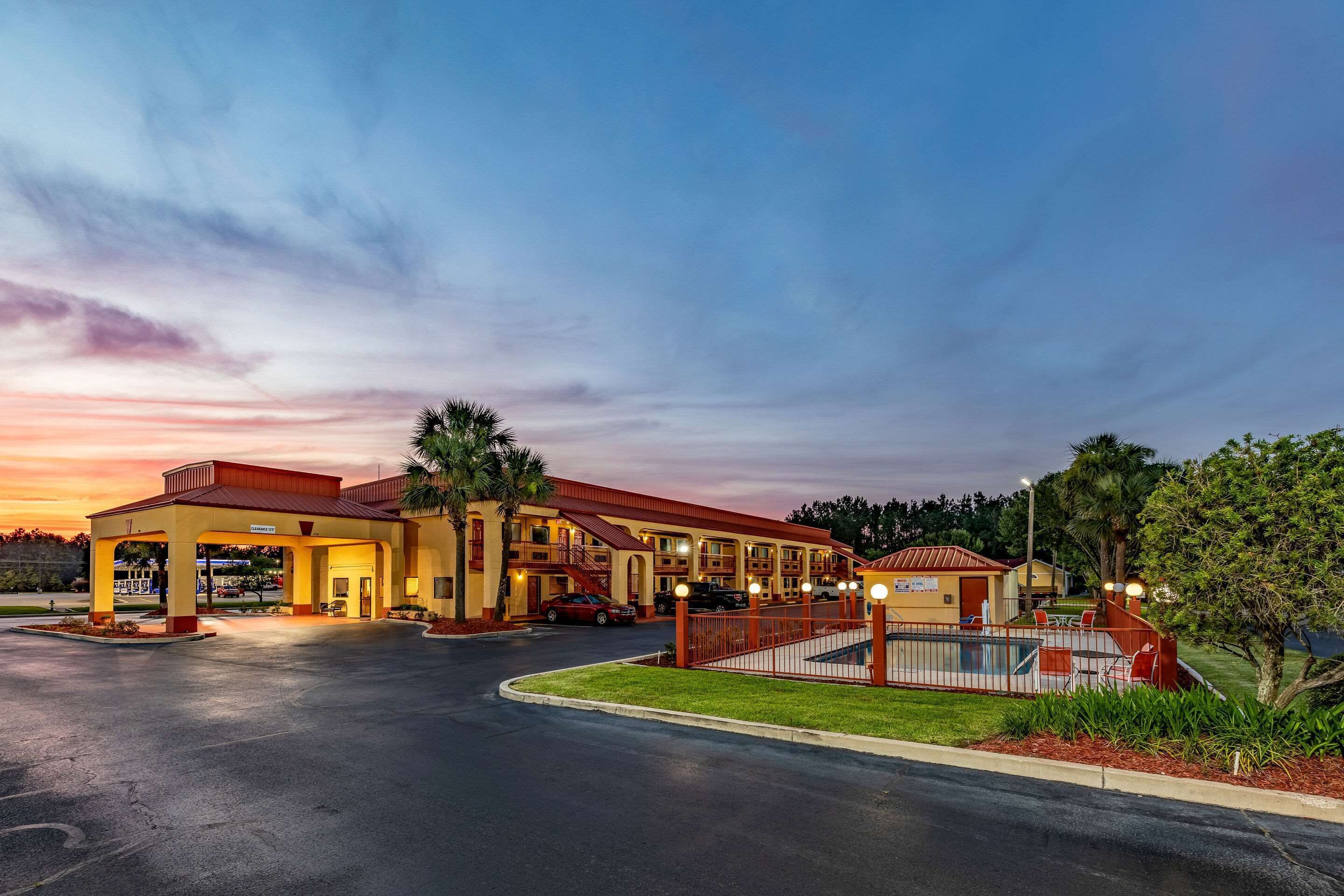 A hotel with a covered parking area, multiple buildings, and a pool area.