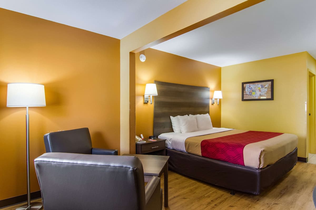 A hotel room with a bed, a desk, a chair, a lamp, and a wall-mounted map.