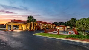 Un hotel con estacionamiento techado, mesas al aire libre y piscina.