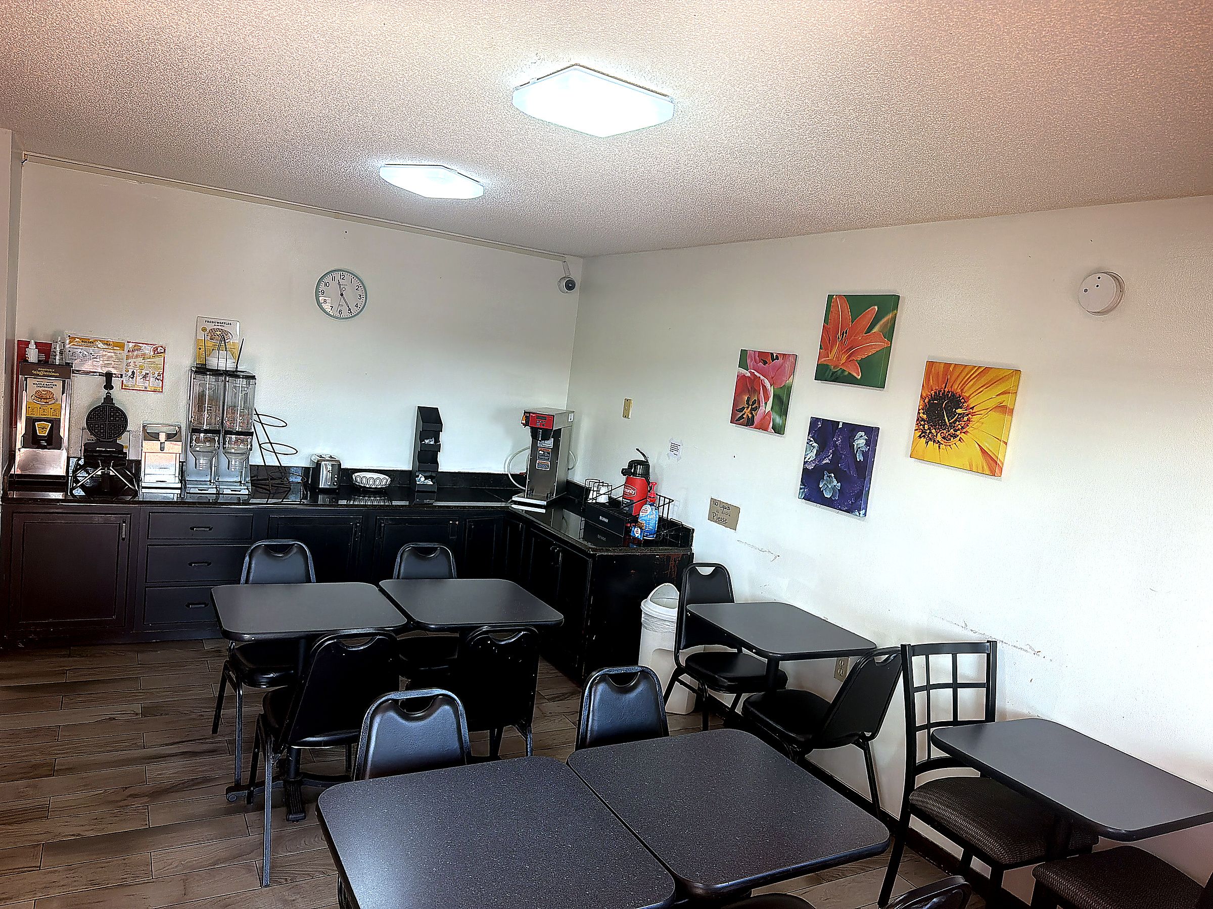 A room with a kitchenette, a clock, and several tables and chairs.