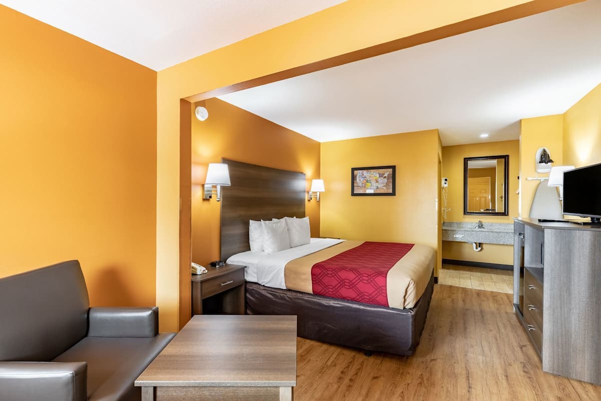 A hotel room with a bed, bedside tables, a desk, a chair, a mirror, and a television.