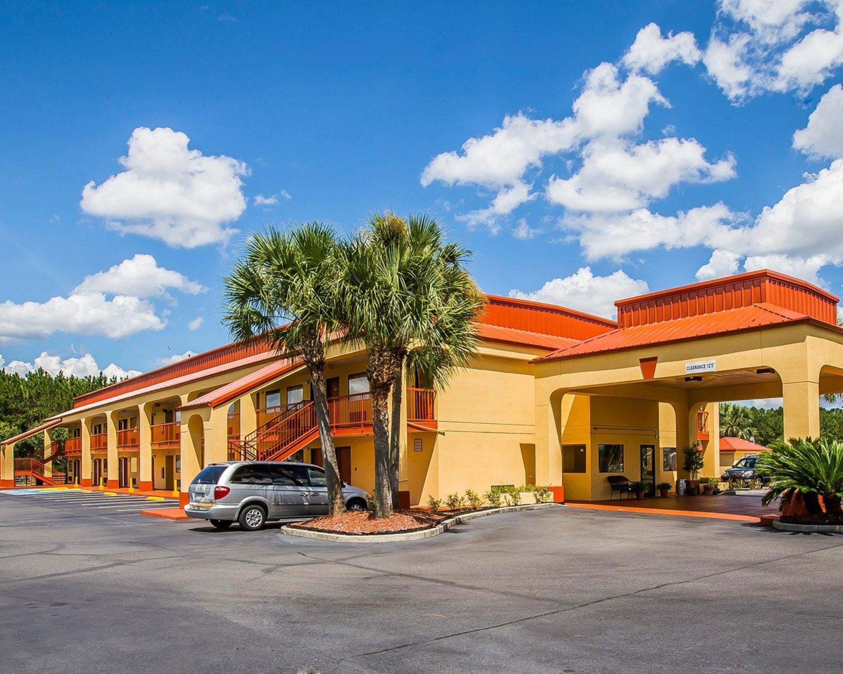 A hotel with multiple balconies, a parking lot, and a palm tree.