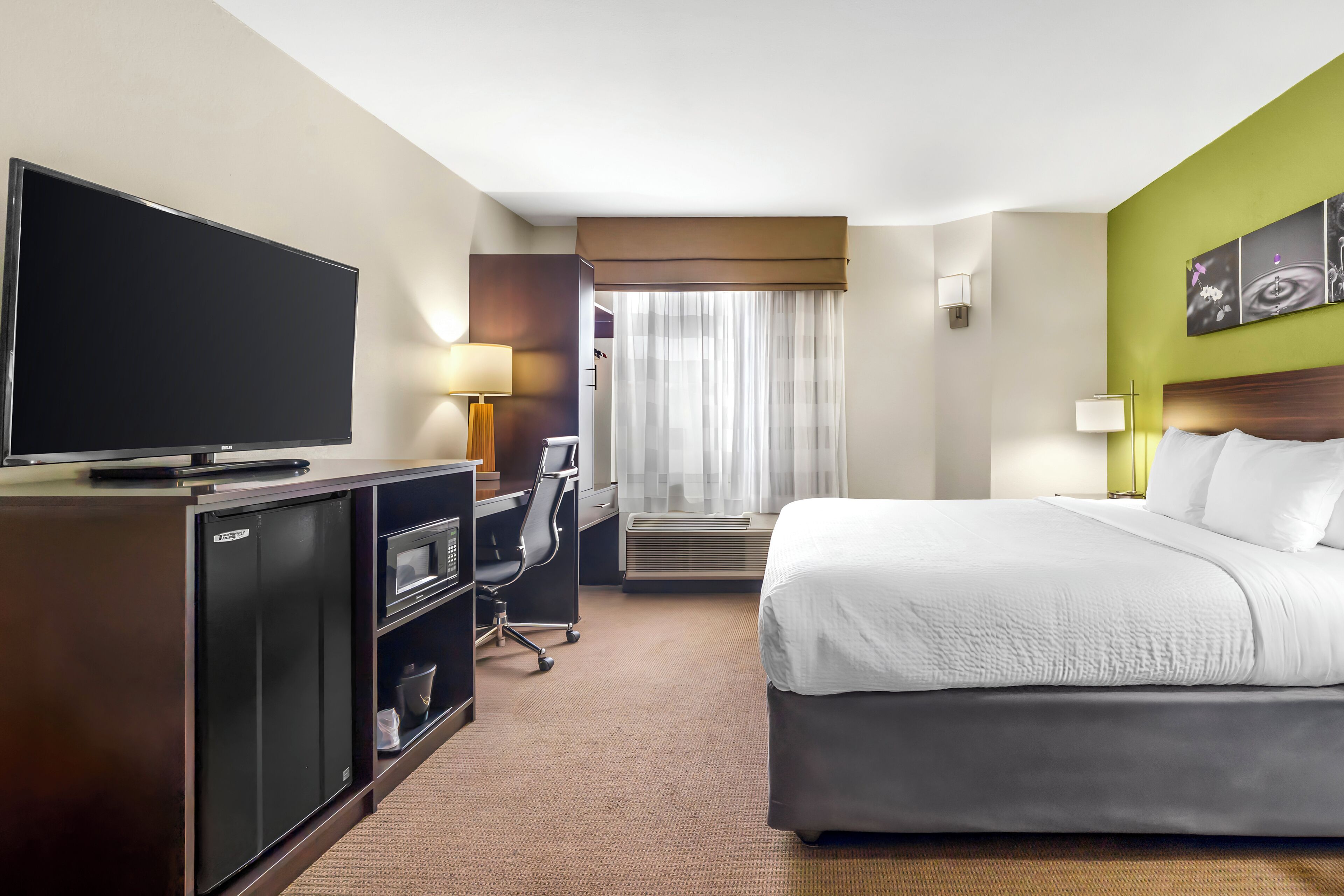 Habitación de hotel con cama, escritorio, computadora, televisor y ventana con cortinas.