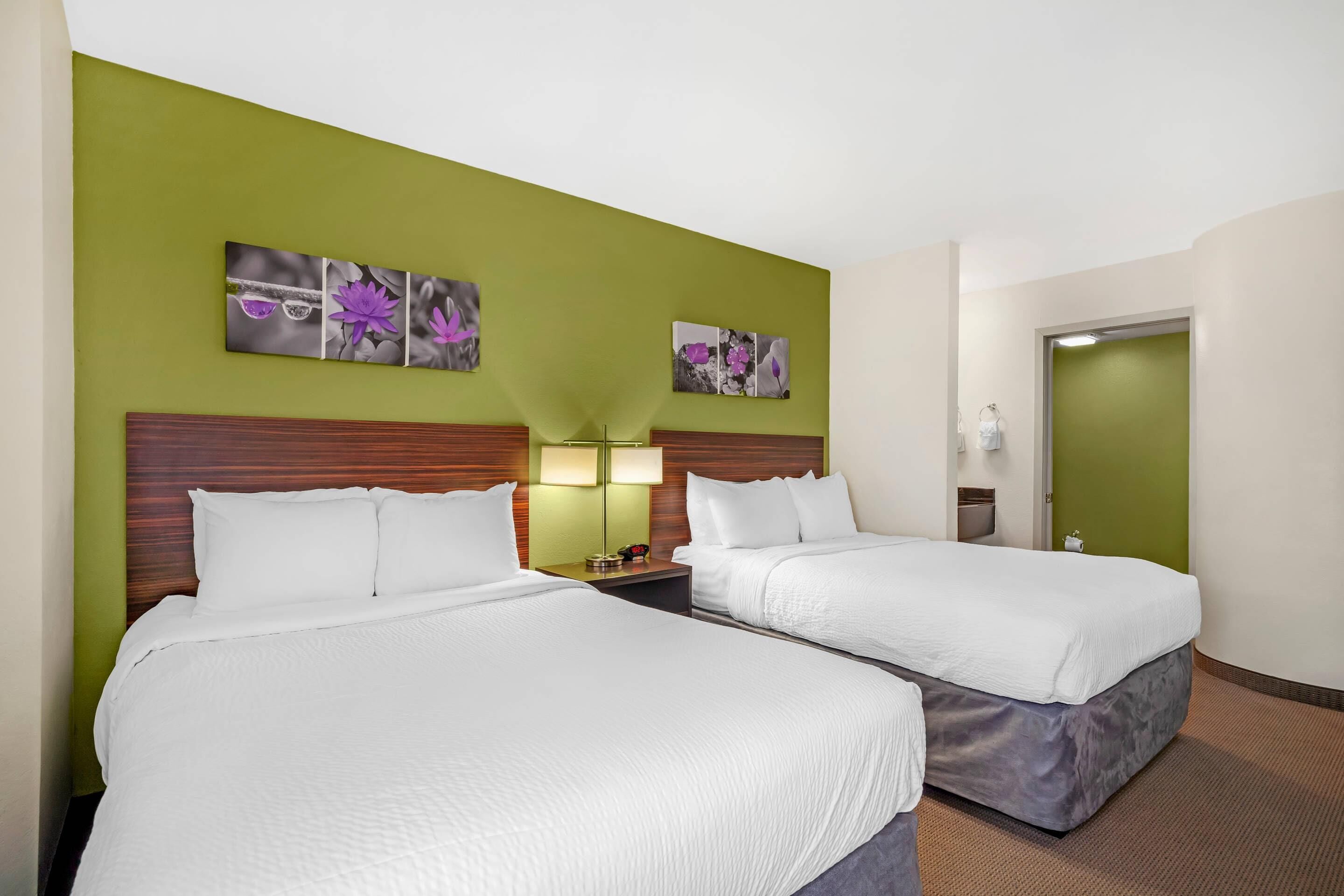 A hotel room with two beds, green walls, and artwork on the wall.