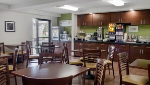 Un restaurant avec des tables et des chaises en bois, un espace cuisine et une vue sur l’extérieur.