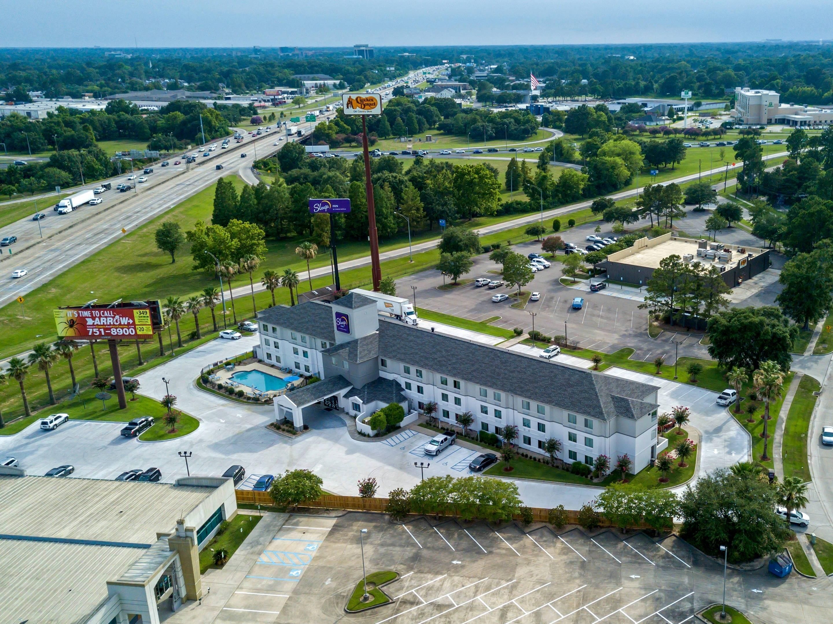 A hotel with a swimming pool, multiple parking lots, and a large road with traffic.