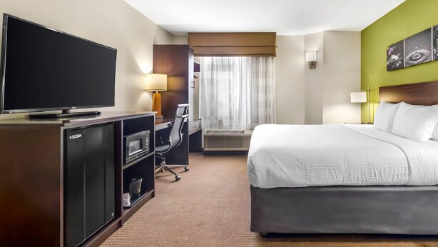Une chambre d’hôtel dotée d’un grand lit, d’un téléviseur à écran plat, d’un bureau avec une chaise, d’un mini-réfrigérateur et d’une fenêtre avec des rideaux.