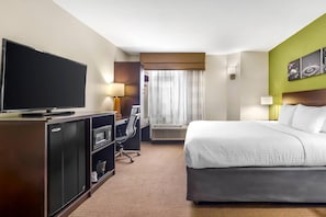 Une chambre d’hôtel dotée d’un grand lit, d’un téléviseur à écran plat, d’un bureau avec une chaise, d’un mini-réfrigérateur et d’une fenêtre avec des rideaux.
