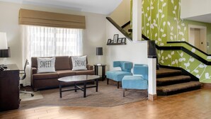Un salon comprenant un canapé, des fauteuils, une table basse et un escalier avec un mur vert.