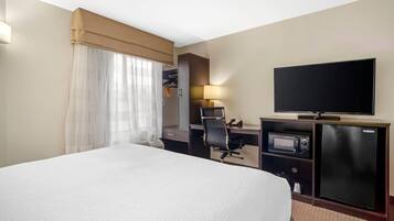 A hotel room with a large bed, a desk with a computer, a television, and a minibar.