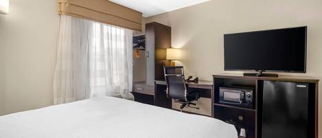 A hotel room with a large bed, a desk with a computer, a television, and a minibar.