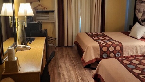 Ein Hotelzimmer mit zwei Betten, einem Schreibtisch mit Lampe, einem Sessel und einem großen Spiegel.