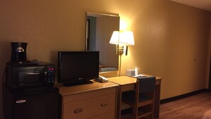 Ein Hotelzimmer mit Schreibtisch, Fernseher, Kaffeemaschine, Lampe und einem Sessel.